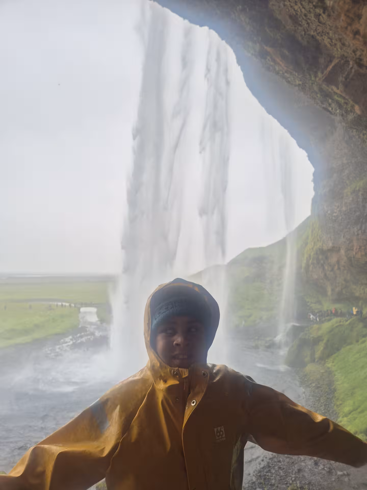 Traveler in yellow rain jacket standing behind Seljalandsfoss waterfall on Iceland South Coast tour