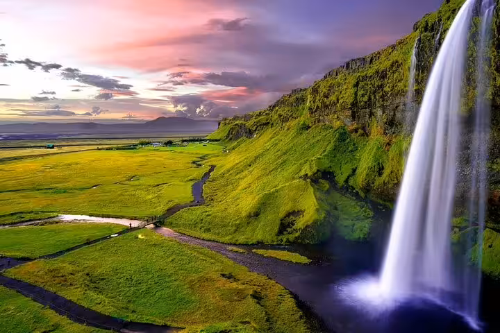 Seljalandsfoss waterfall cascading over green cliffs onto Iceland's south coast plains at sunset