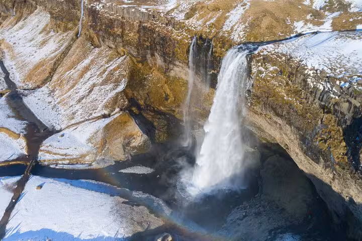 Aerial view of Seljalandsfoss waterfall with rainbow and snow-covered Iceland south coast landscape