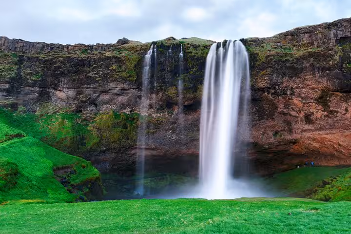 Seljalandsfoss waterfall cascading over mossy cliffs onto green meadow on Iceland's South Coast
