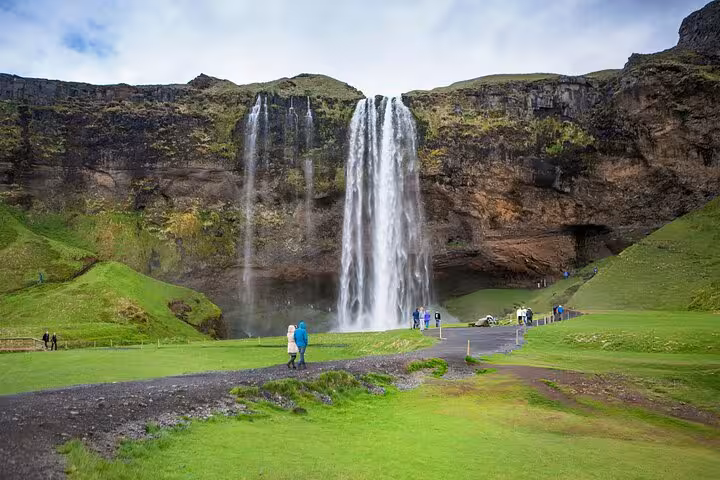 Tourists walking toward Seljalandsfoss waterfall on Iceland's South Coast with lush green landscape