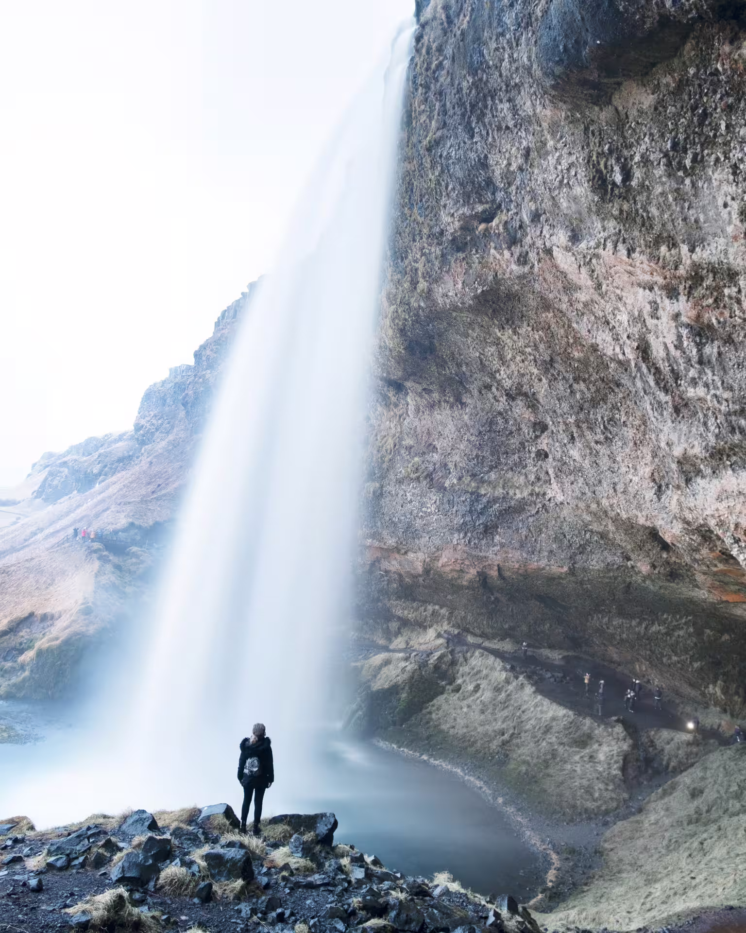 Person standing on rocks beside towering Seljalandsfoss waterfall on Iceland's South Coast
