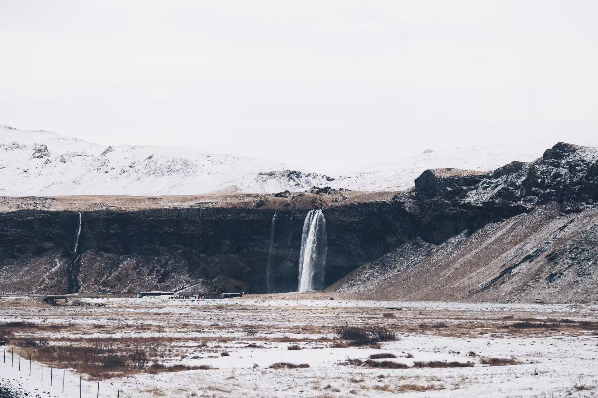 Seljalandsfoss waterfall cascading down black cliffs with snow-covered landscape on Iceland's South Coast