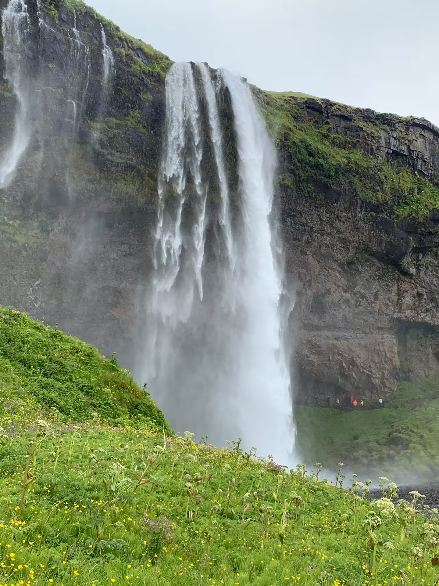 Powerful waterfall cascading down mossy cliffs with tourists standing beneath on a private super jeep tour