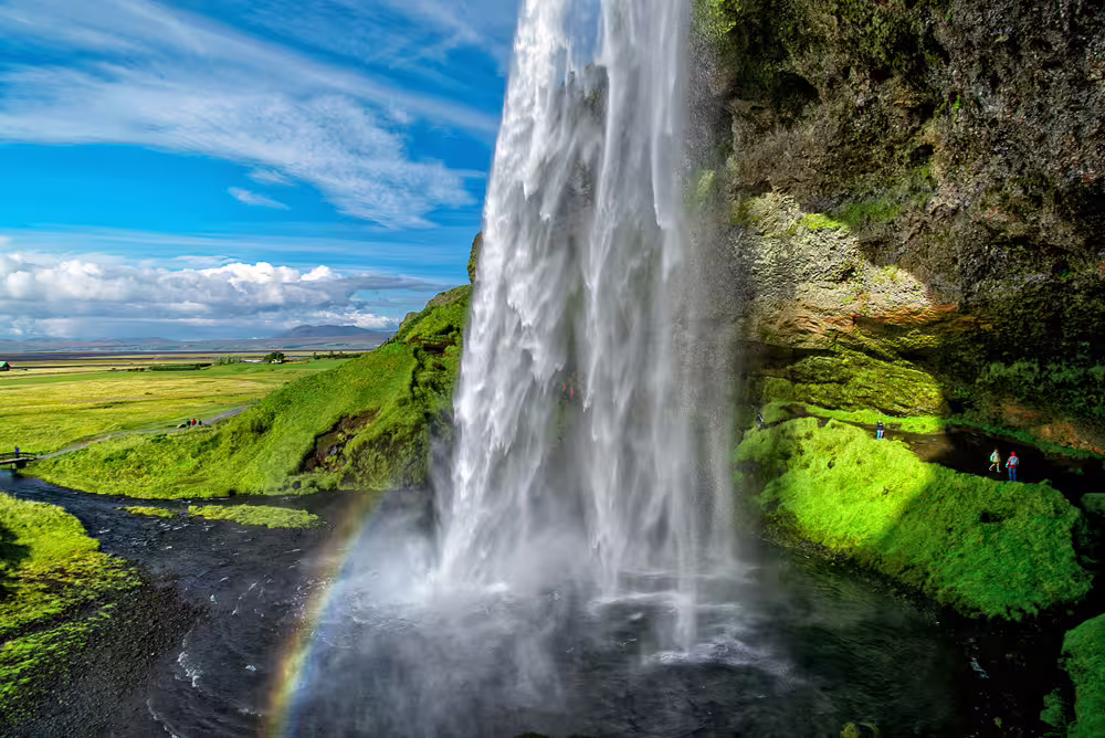 Seljalandsfoss waterfall with rainbow and green landscape on Iceland's South Coast tour
