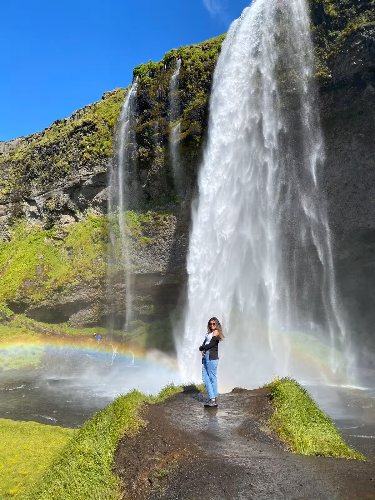 Traveler standing beside majestic Seljalandsfoss waterfall with a rainbow on South Coast Iceland private day trip from Reykjavik
