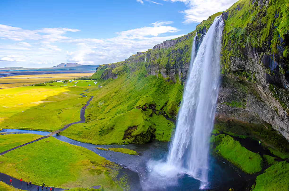 Seljalandsfoss waterfall cascading down green cliffs with Icelandic plains stretching to the horizon