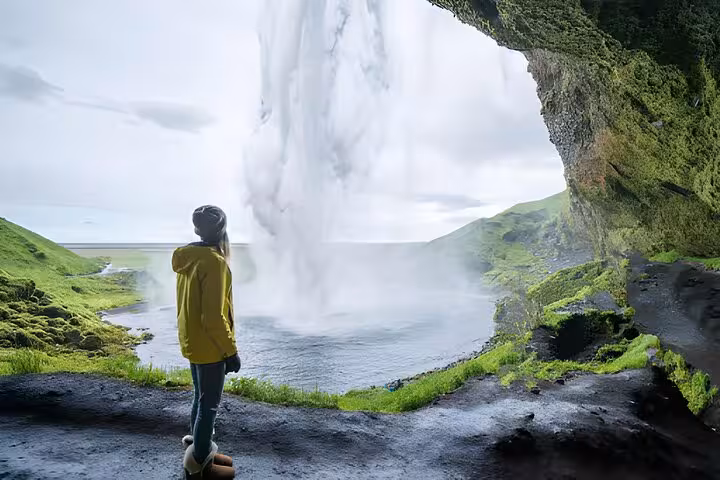 Traveler in yellow jacket viewing Seljalandsfoss waterfall from behind on Iceland's South Coast