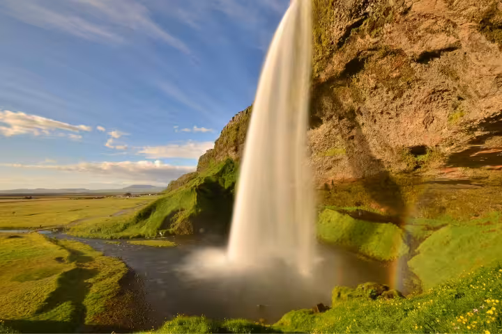 Seljalandsfoss waterfall cascading into green valley with rainbow on Iceland's south coast
