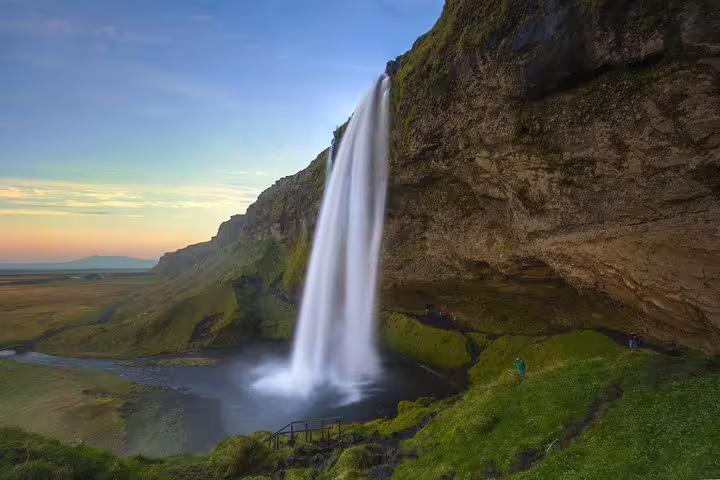Seljalandsfoss waterfall cascading over mossy cliffs with golden hour sky and green Icelandic plains