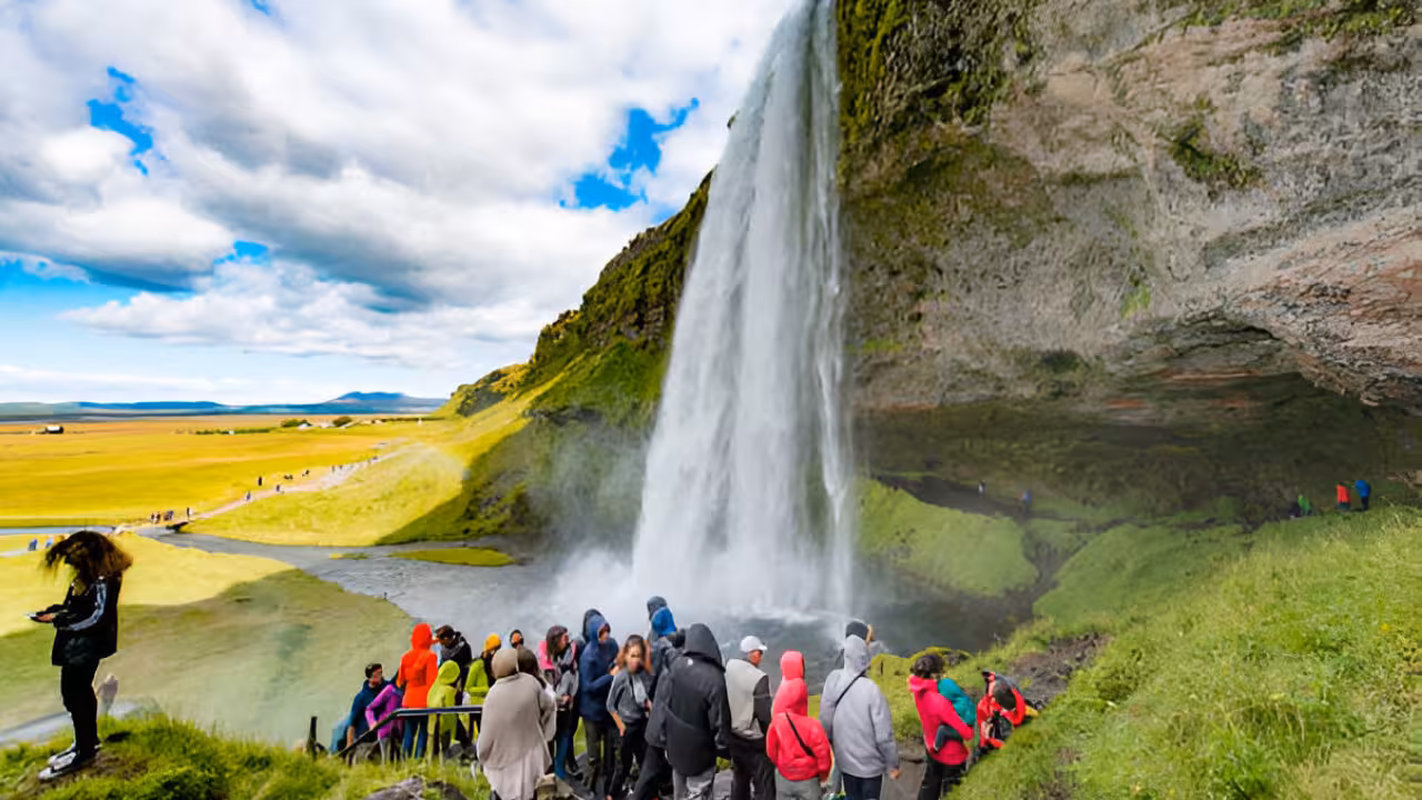 Tourists viewing Seljalandsfoss waterfall on Iceland's South Coast with green plains in background