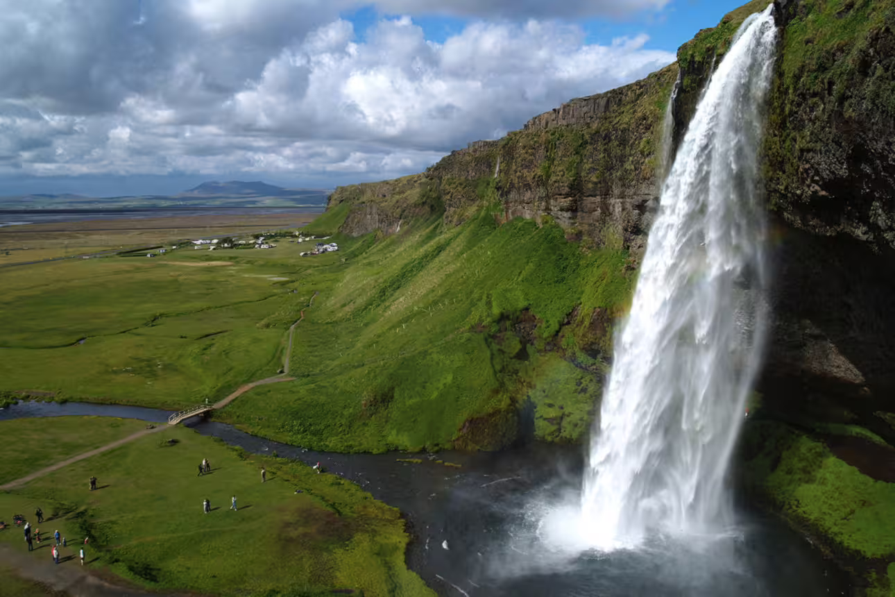 Seljalandsfoss waterfall cascading down green cliffs on Iceland's South Coast with visitors below