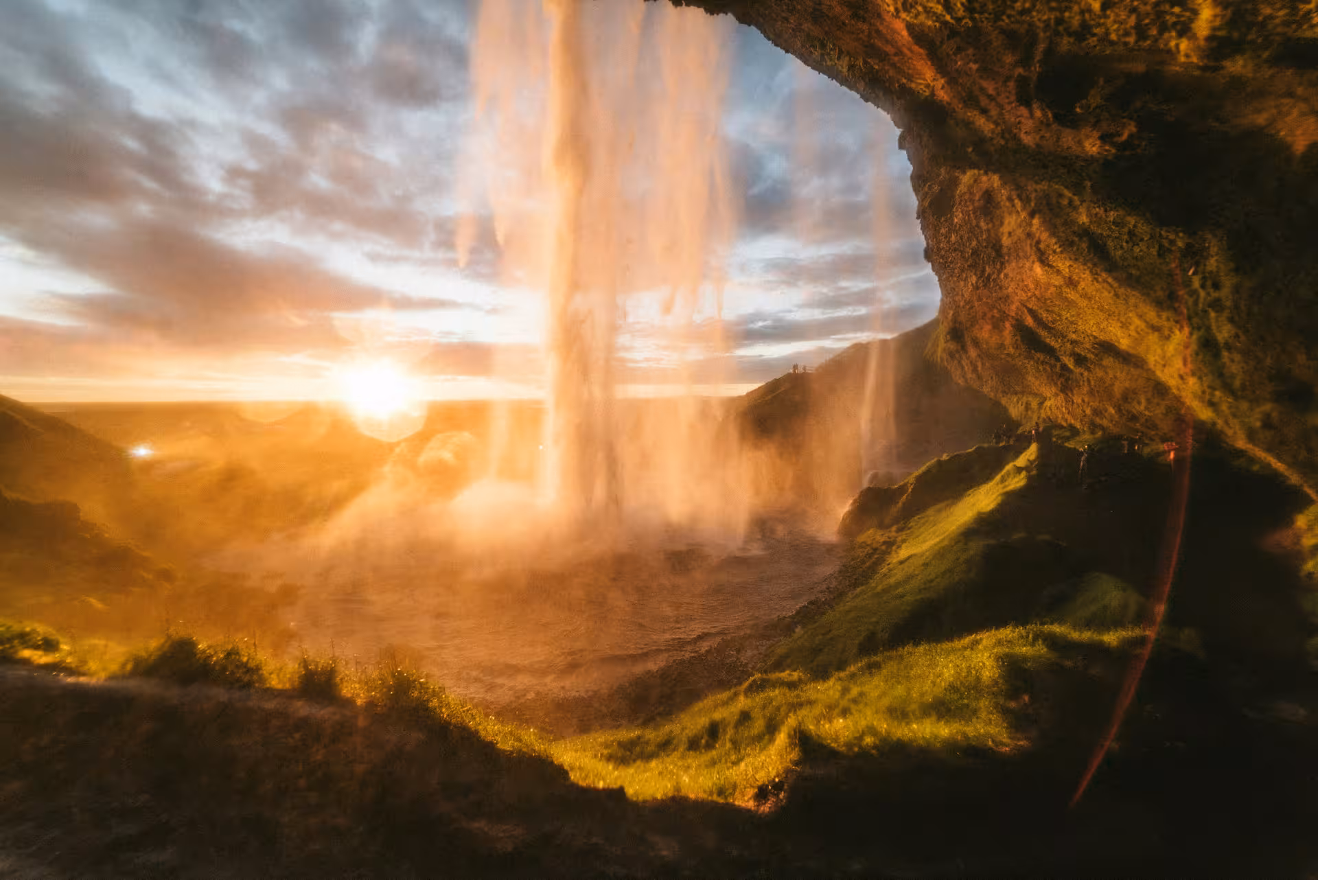 View from behind Seljalandsfoss waterfall at golden sunset on Iceland's South Coast