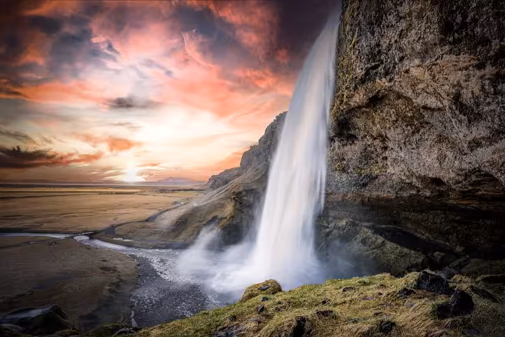 Seljalandsfoss waterfall cascading over cliffs at sunset on Iceland's South Coast near black sand beach