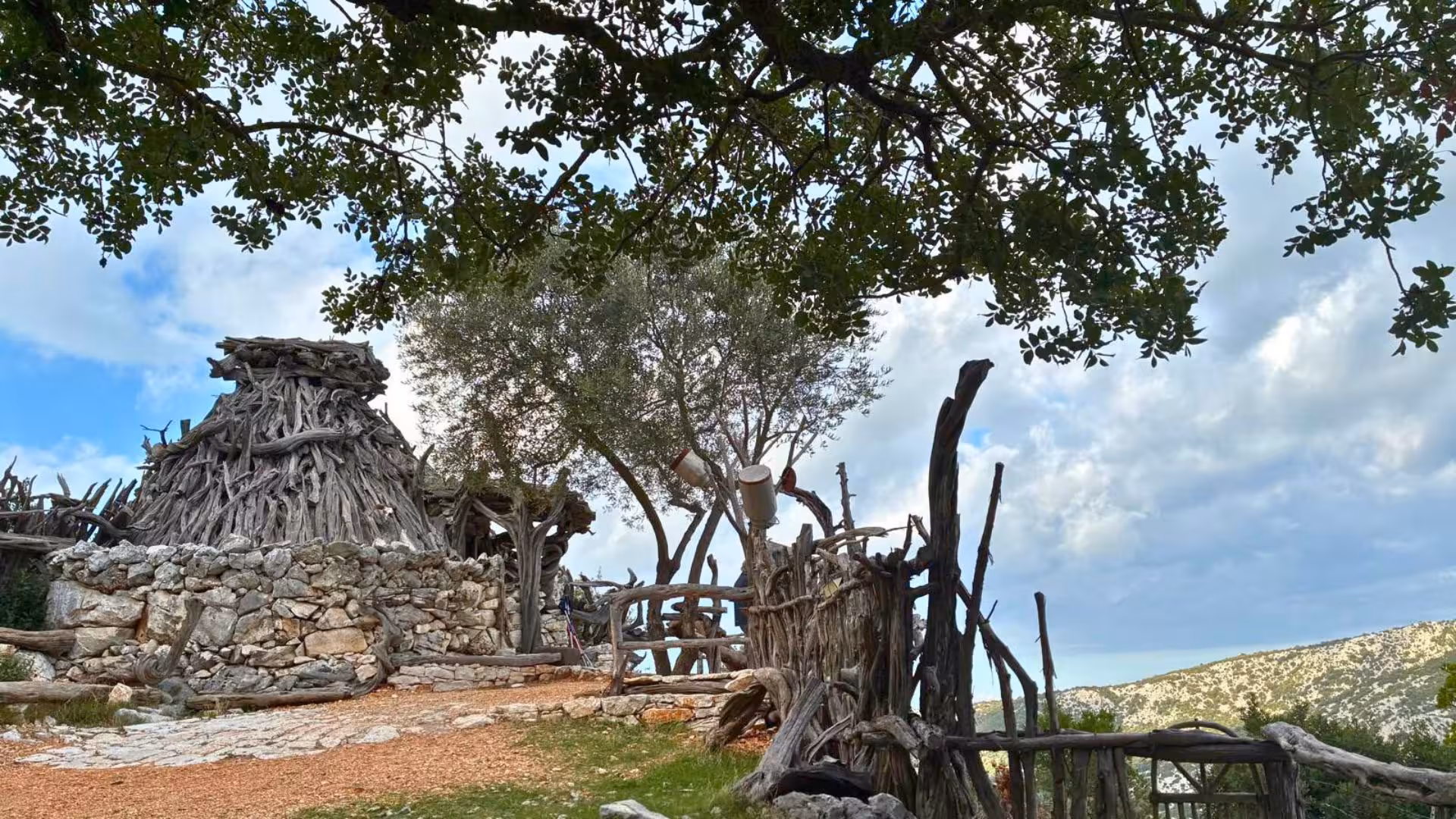 Rustic stone and wood structures under trees on the Selvaggio Blu hiking trail in Sardinia.