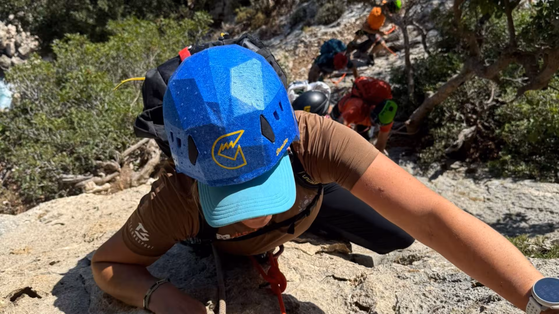 Climber scaling a steep rock face on the Selvaggio Blu trek, surrounded by lush greenery.