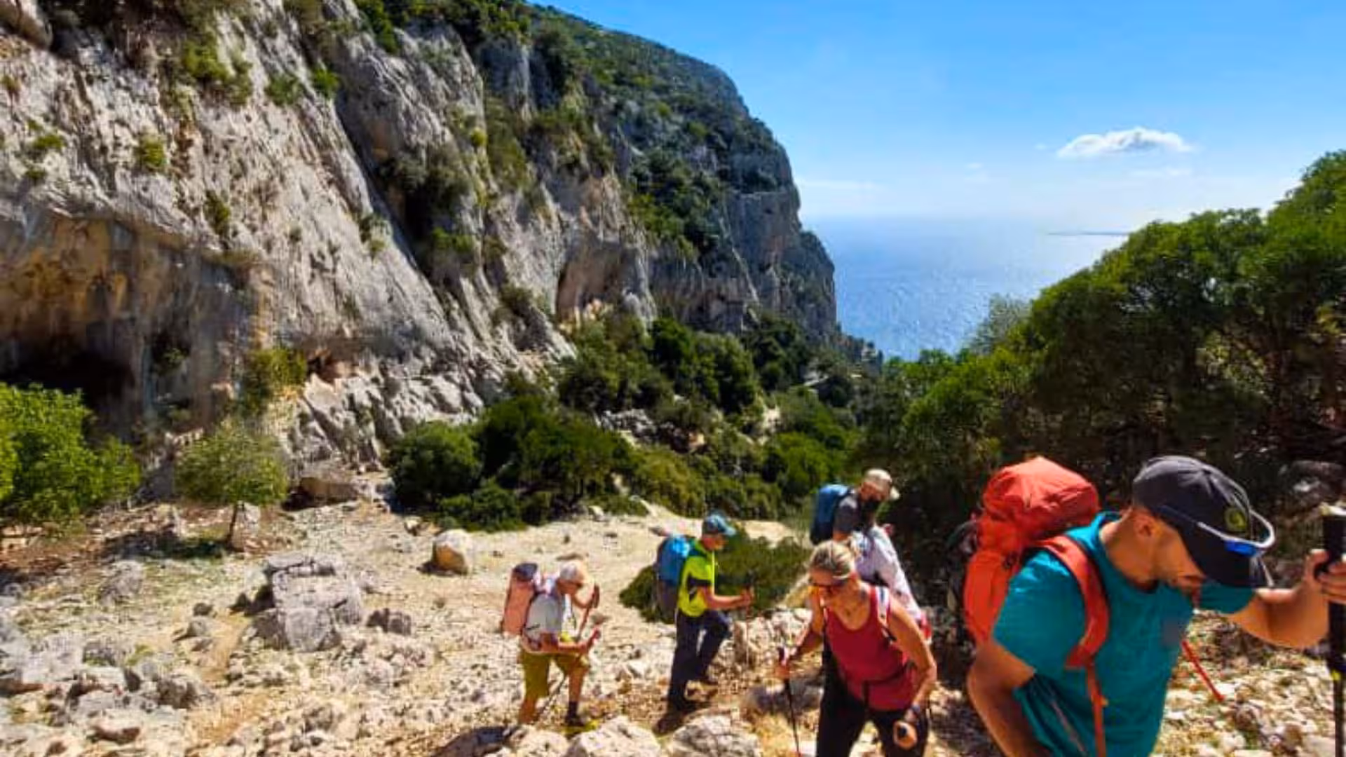 Group of hikers ascending rocky path with ocean view on Selvaggio Blu trek from Arbatax.