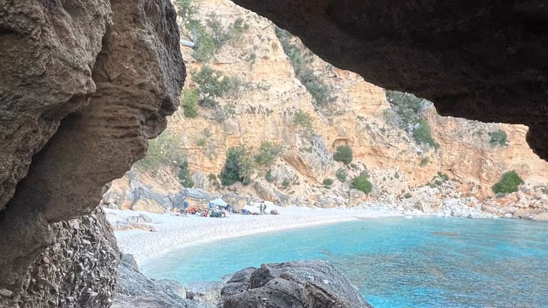 Breathtaking view of a secluded beach and turquoise sea from a rocky cave on the Selvaggio Blu trek.
