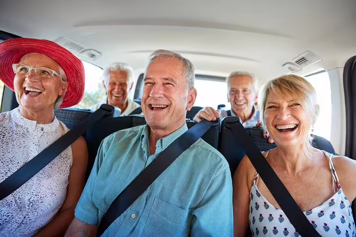 Group of five happy senior travelers laughing together inside a private transfer vehicle