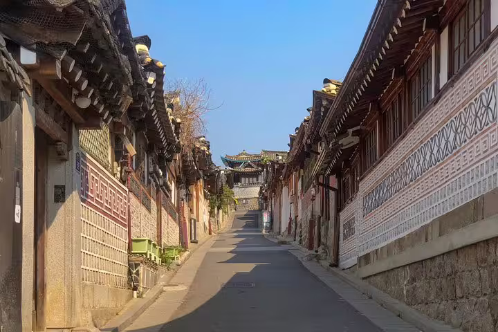 Narrow traditional hanok alley in Seoul with tiled rooftops and decorated stone walls under clear blue sky