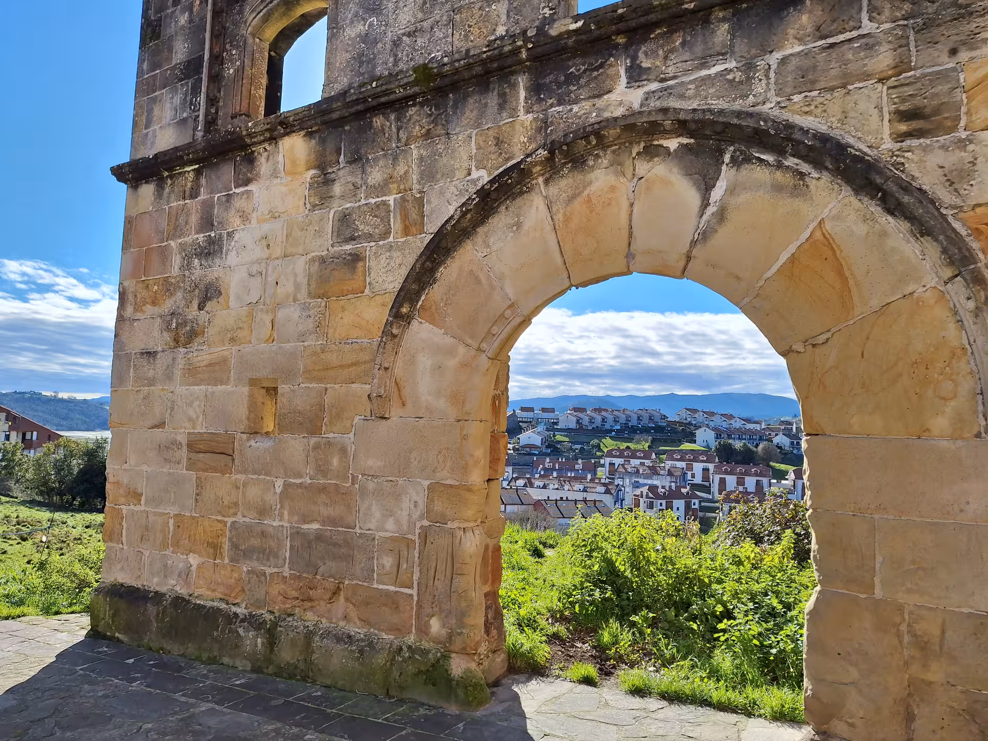 Historic stone archway overlooking San Vicente de la Barquera's picturesque townscape and lush greenery.