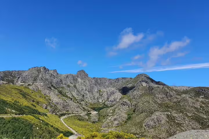 Panoramic vista of Serra da Estrela's rugged mountains and winding road against a vibrant blue sky.