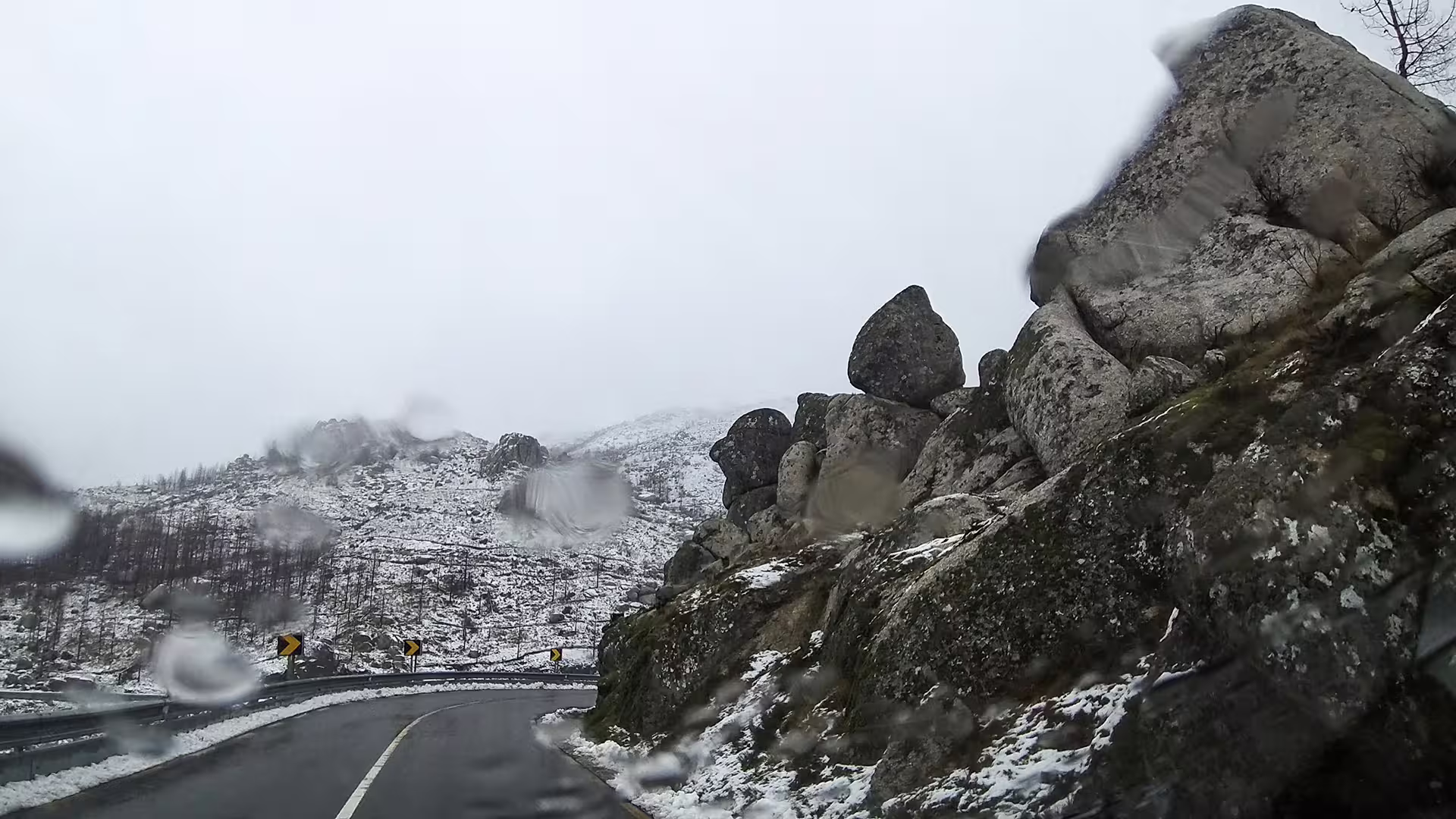 Scenic view of a winding road through snow-dusted Serra da Estrela Park, highlighting rugged rock formations and winter landscape.