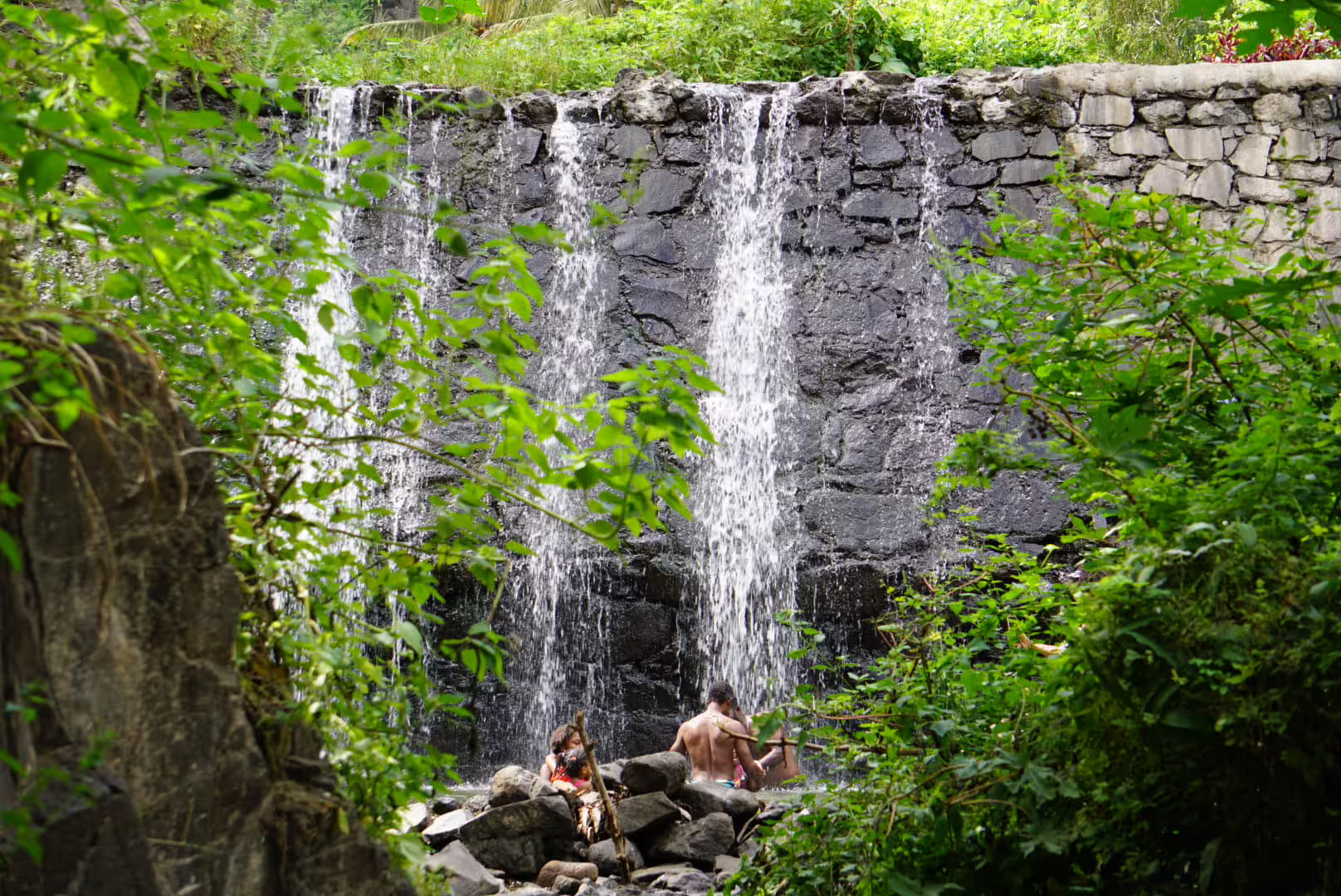 Tourists enjoy a refreshing swim under a cascading waterfall surrounded by lush greenery in Serra Malagueta.