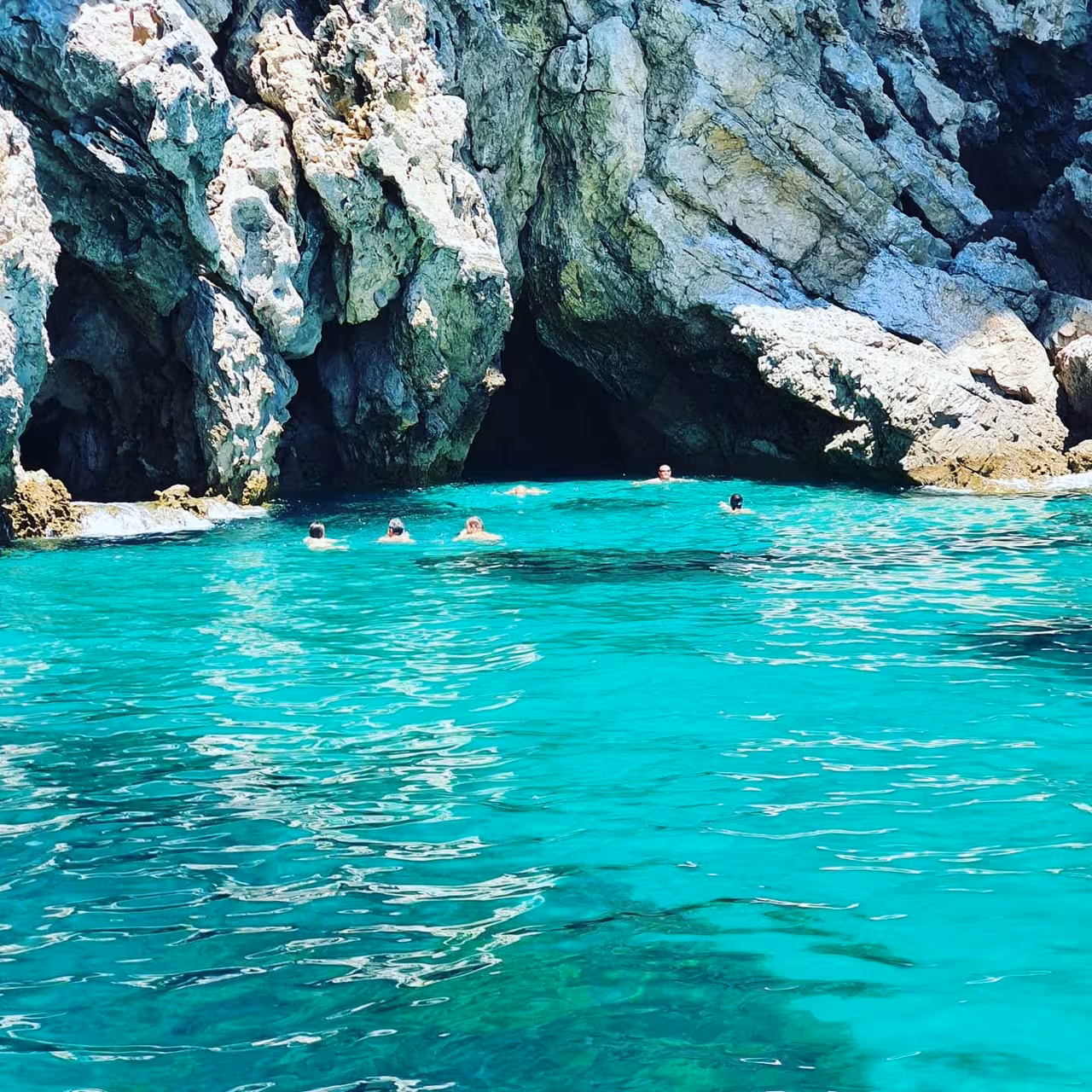 Swimmers enjoying crystal-clear lagoon by sea caves on a Sesimbra boat tour, Arrábida Natural Park, Portugal