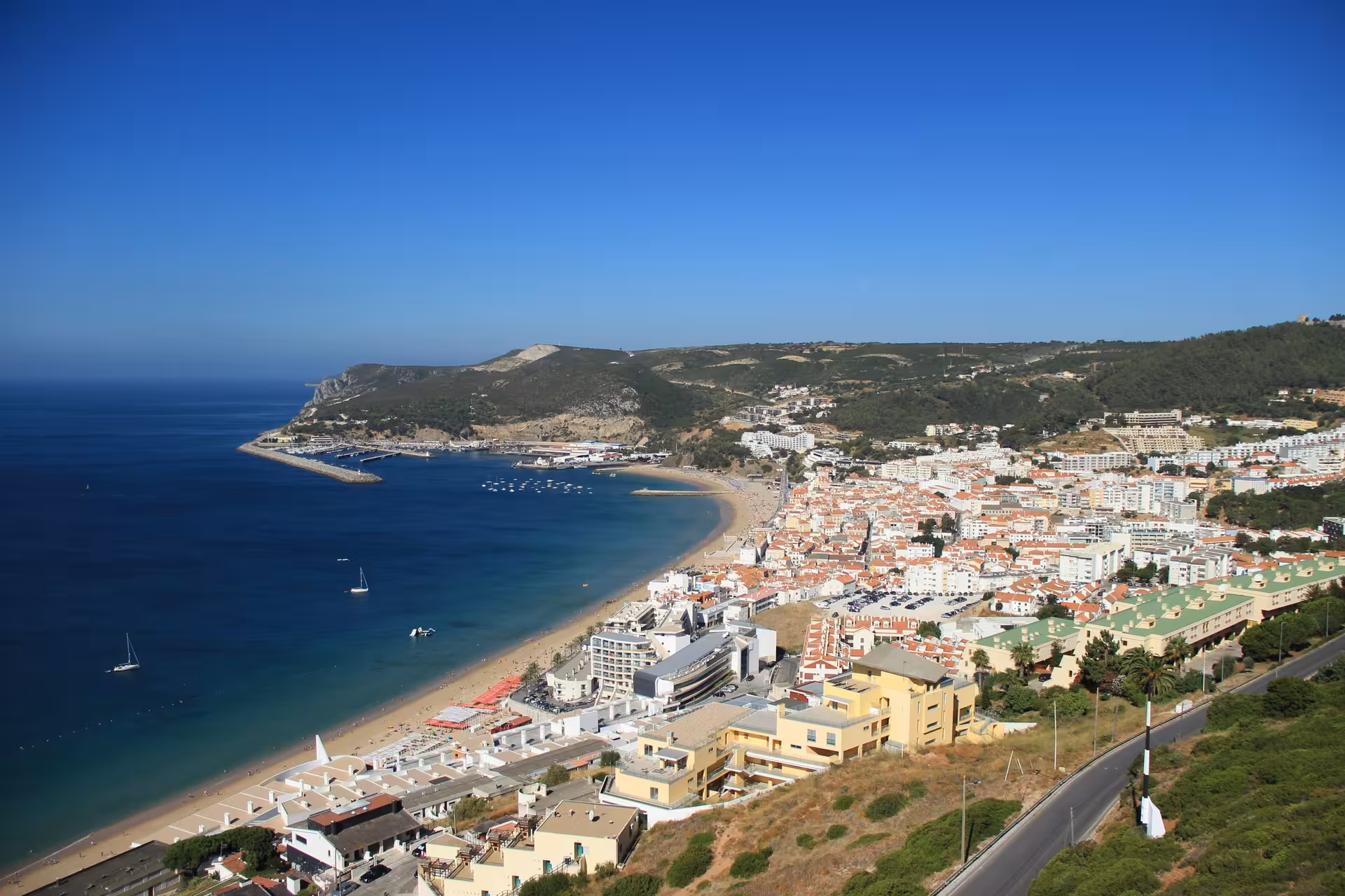 Aerial view of Sesimbra's coastline with sandy beaches, blue waters, and scenic hills on the Lisbon day tour.
