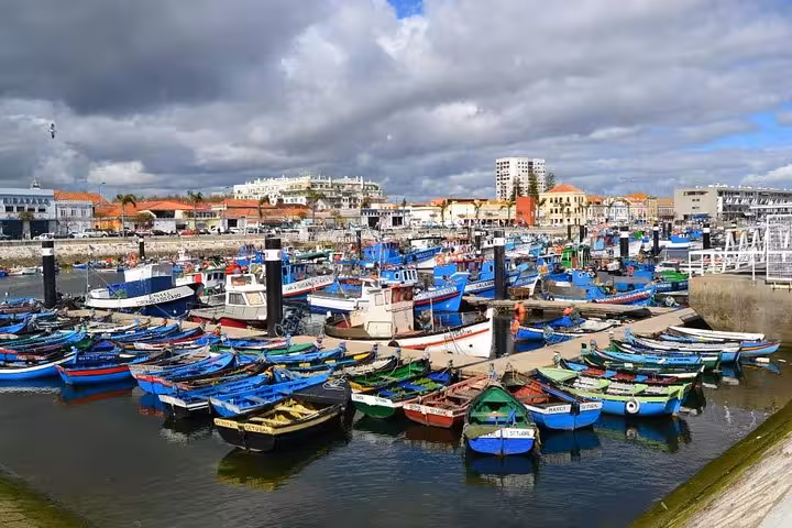 Colorful fishing boats docked in the vibrant Sesimbra harbor against a backdrop of coastal town buildings.