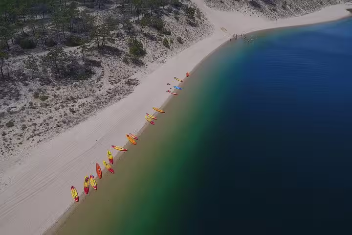 Aerial view of vibrant kayaks lined up on the sandy shore of a tranquil lagoon in Sesimbra, ideal for an easy kayaking experience.
