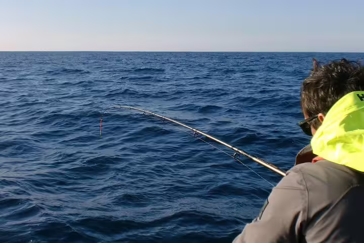 Angler in bright life jacket fishing in the deep blue waters of Sesimbra on an all-inclusive sport fishing tour.