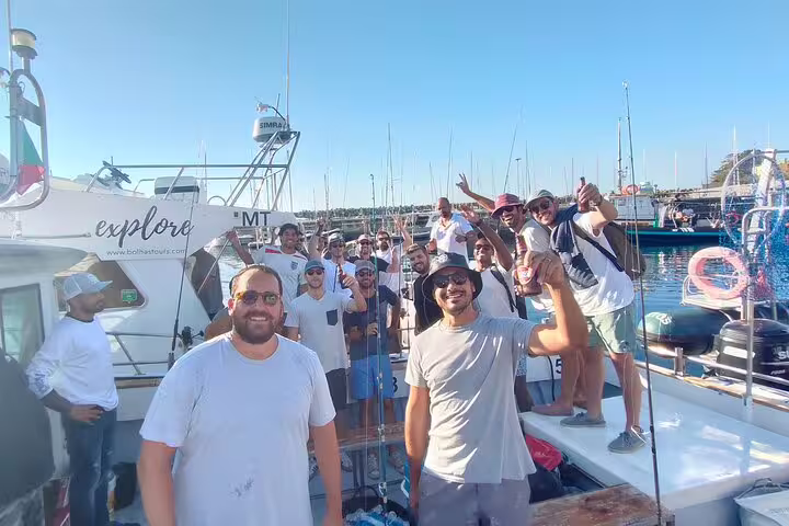 A group of excited anglers enjoying a sunny all-inclusive sport fishing tour on a boat in Sesimbra's vibrant marina.