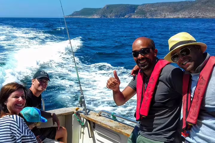 Group enjoying a sport fishing tour in Sesimbra, Portugal, on a sunny day, with life vests and scenic ocean backdrop.