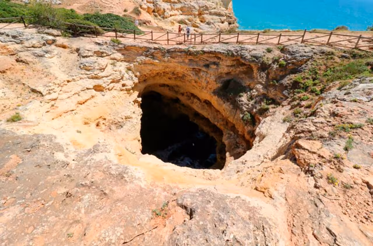 Natural sea cave sinkhole on Algarve cliffs with tourists viewing stunning coastal scenery on Seven Hanging Valleys trail