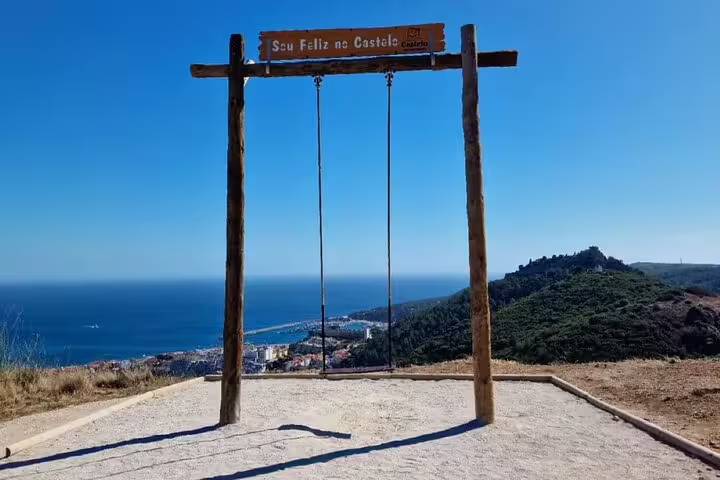 Panoramic view from a hilltop swing overlooking Setúbal's coastline with a castle and ocean in the distance.