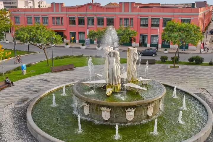 Experience the elegance of Setúbal's fountain with classical statues and water features set against a vibrant architectural backdrop.