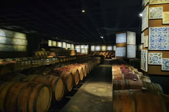 Explore the atmospheric wine cellar with rows of wooden barrels aging Setúbal Moscatel, perfect for wine enthusiasts.
