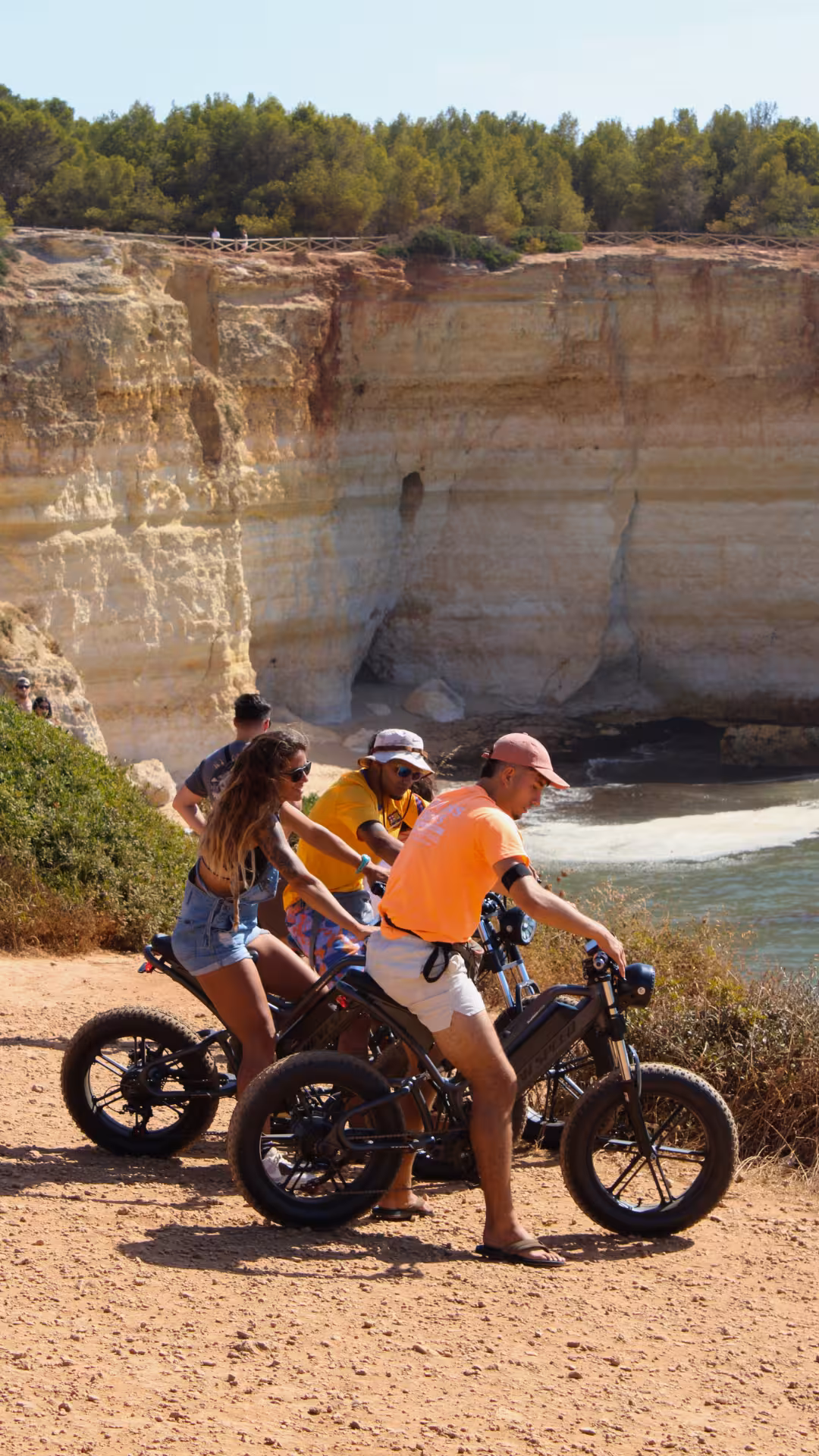 Friends ride electric bikes along the Seven Hanging Valleys coastal trail, overlooking Algarve cliffs and turquoise sea views