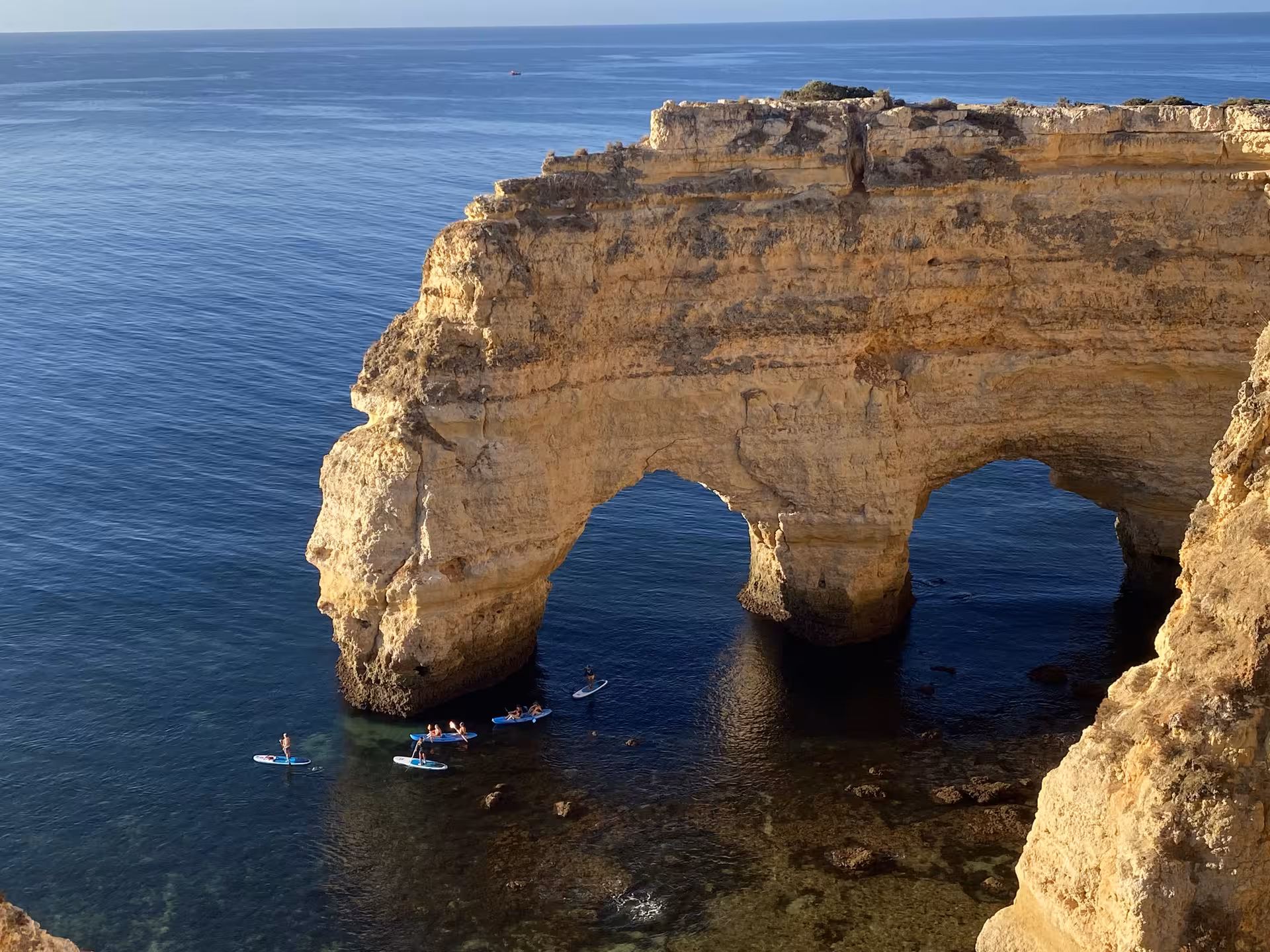 Golden limestone sea arch at Praia da Marinha with paddleboarders below on the Seven Hanging Valleys hike Algarve