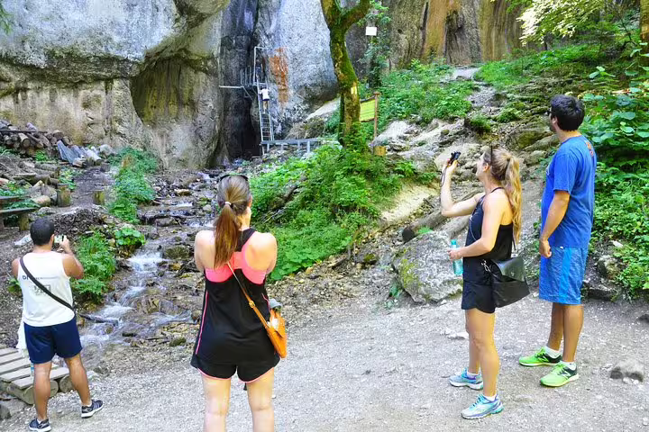 Tourists photographing waterfall and rocky canyon entrance at Seven Ladders Canyon near Brasov
