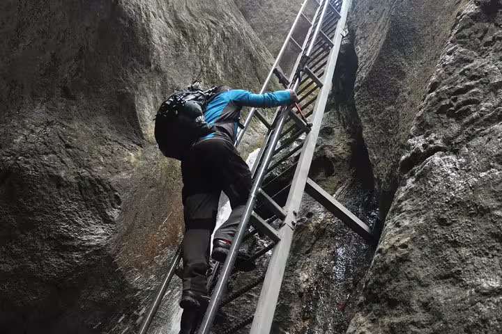 Hiker climbing metal ladder through narrow rocky canyon passage at Seven Ladders Canyon