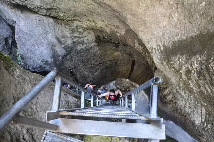 Hikers climbing steep metal stairs through Seven Ladders Canyon rock passage near Brasov