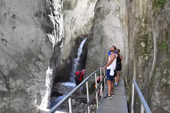 Hikers on metal walkway admiring waterfall inside Seven Ladders Canyon narrow gorge near Brasov