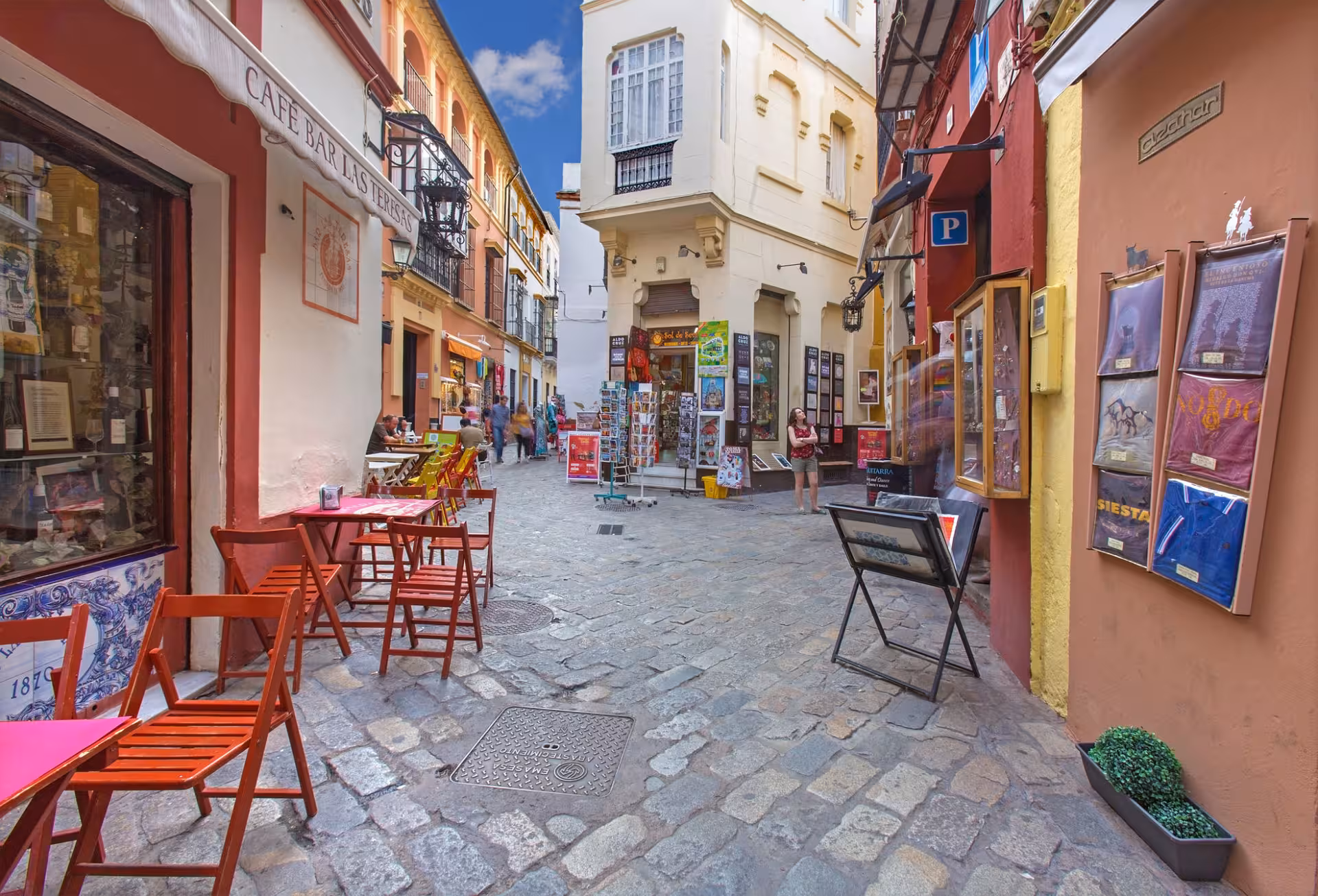 Charming cobblestone street in Seville's old Jewish quarter with outdoor cafes and colorful buildings, ideal for guided tours.