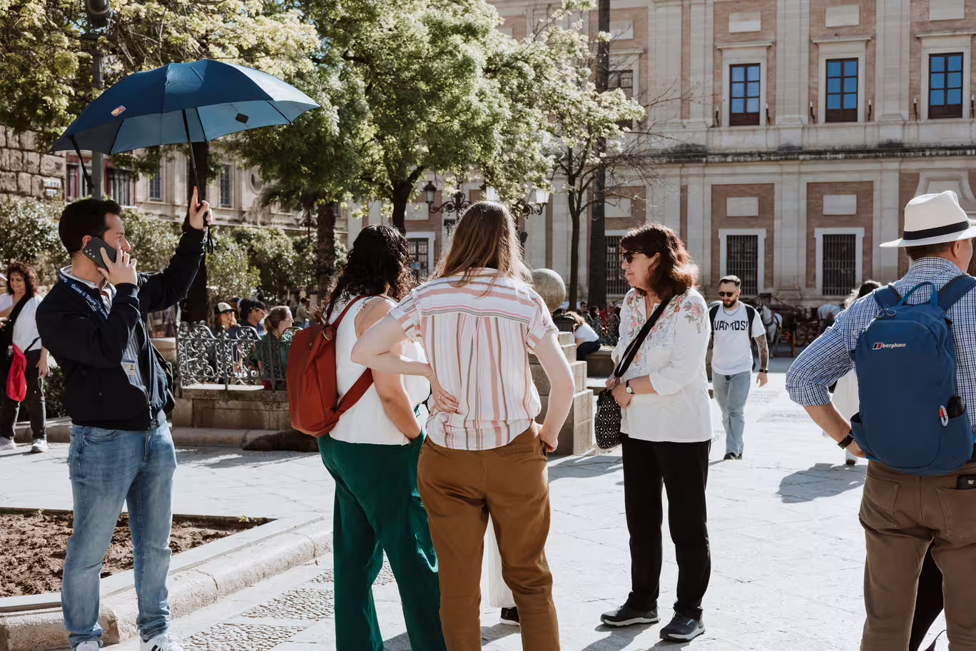 Tour group exploring Seville's Santa Cruz neighborhood with guide holding umbrella under sunny skies.