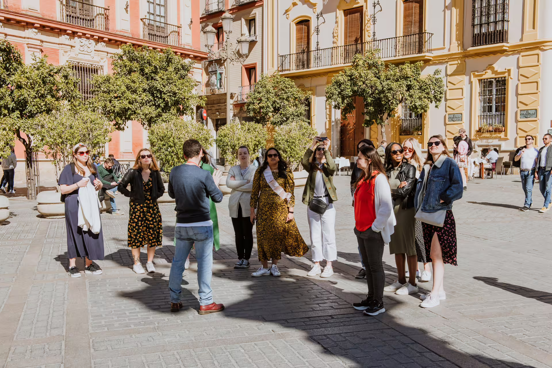 Tourists gathered around a guide in Seville's vibrant Santa Cruz district, discovering the Jewish Quarter's history.