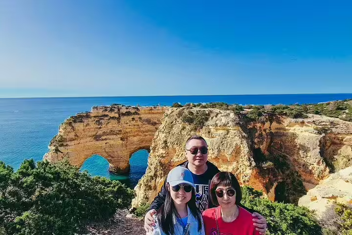 Family enjoying scenic Algarve coastline views on Seville to Lisbon transfer tour, highlighting natural arches and blue sea.