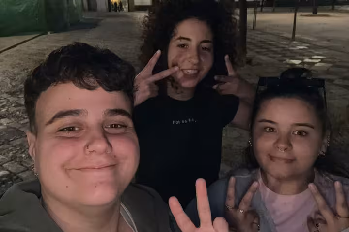 Three young friends posing with peace signs at night in Seville city streets